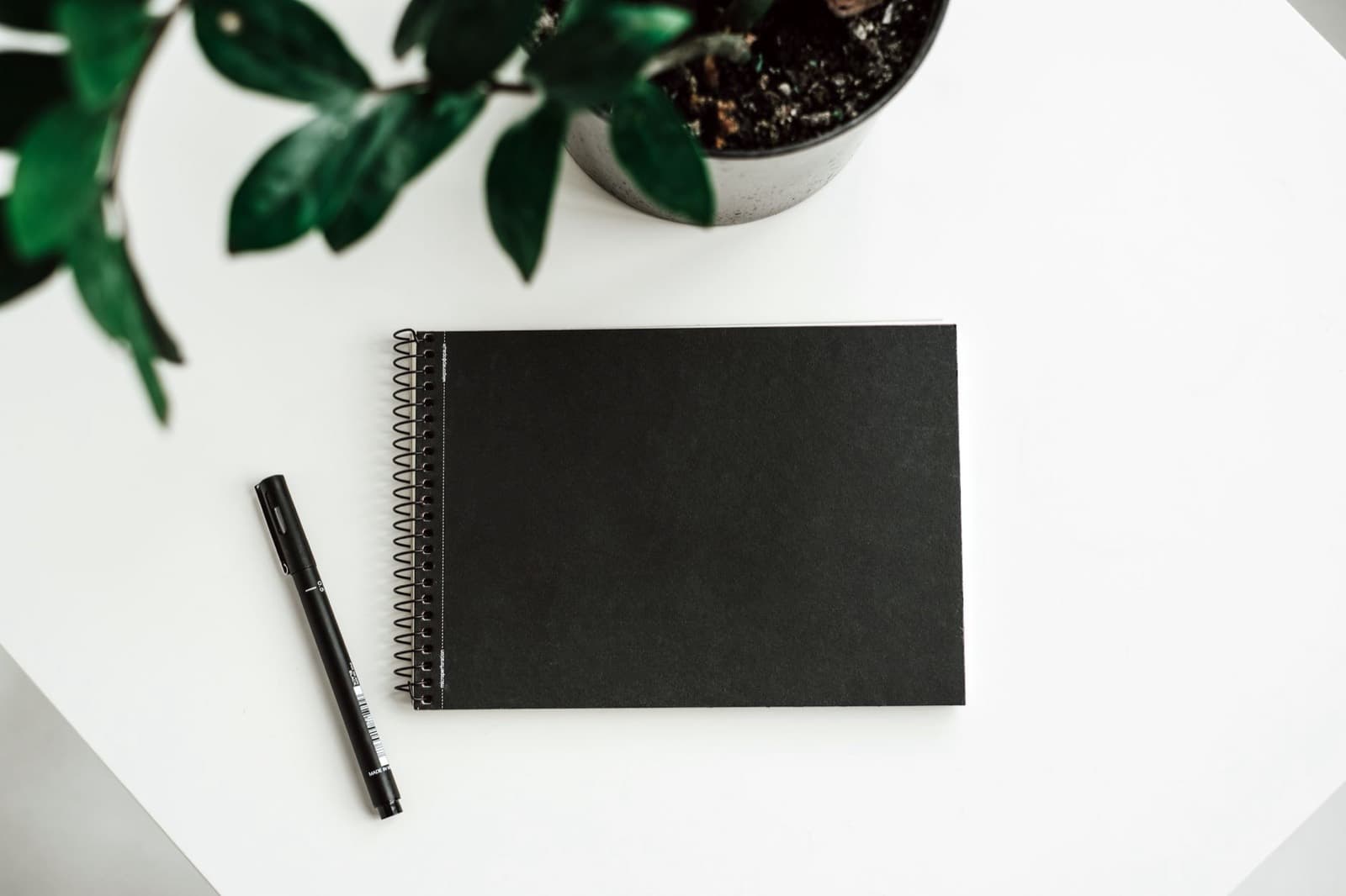 A closed black notebook and pen on a white desk